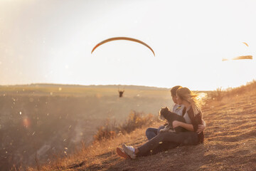 A happy family with a dog are sitting on the top of the hill, watching the paragliders fly in the...