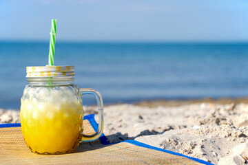 A yellow cocktail in a fashionable mug stands on the seashore on a green cloth. Sunny day, golden...
