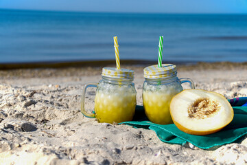 A yellow cocktail in a fashionable mug stands on the seashore on a green cloth. Melon smoothie. Healthy drink.
