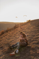A young man hugs a beautiful girl from behind, the couple admire the sunset from the top of the hill. The lovers are sitting, hugging the little schnauzer. Happy family travels with a dog on an autumn