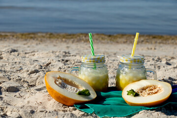 A yellow cocktail in a fashionable mug stands on the seashore on a green cloth. Melon smoothie. Healthy drink.
