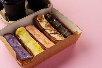 Box of eclairs with takeaway coffee cups on pink background