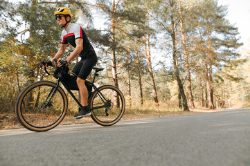Cyclist in a sport outfit rides a bicycle on a forest road in the autumn season. Ьan rides a...