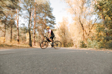 Background. Blurred photo, focus on asphalt. Asphalt road in the woods and a cyclist walking on a bicycle in sports gear. Cyclist rides through the city in the autumn forest.