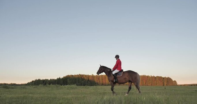 In the general photo, the camera moves with the help of a steadicam along with a driver in a dress red jacket, white trousers and four high boots, galloping across the field in the rays of the setting
