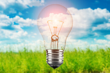 Glowing light bulb on blue sky and green meadow background