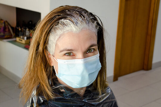 Retrato de una mujer joven y rubia con el tinte puesto y mascarilla en el interior de una peluquer&iacute;a