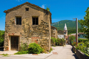 Fototapeta na wymiar Historic buildings in Podnanos, a village in the upper Vipava Valley in the Vipava Municipality in the Primorska region of Slovenia. The bell tower of parish church of Saint Vitus is in the background