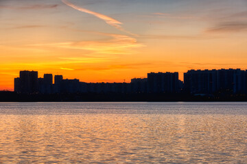 Silhouette of urban buildings against the backdrop of the sunset reflected in the water