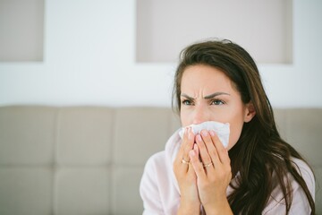 Female covering her face while sneezing sitting on the bed
