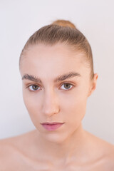 Close-up portrait of a blonde girl with nude makeup, hair gathered in a bun, naked against a gray wall. Natural beauty concept without surgery. Clean face, well-groomed skin, healthy appearance. 
