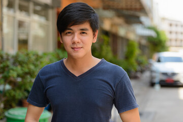Portrait of young handsome Asian man outdoors