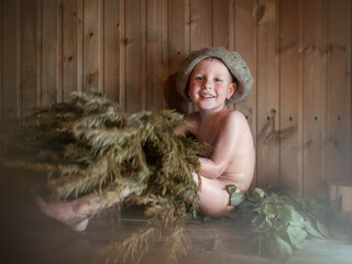 Four-year-old naked boy in hat with silver-fir broom in hands in Russian bath-house. Smiling little child is taking steam-bath at sauna. Authentic shot © fascinadora