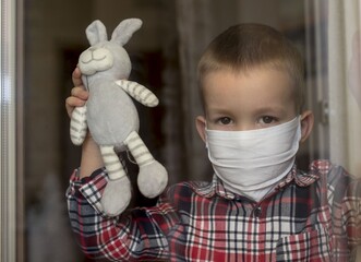 Adorable little boy wearing a medical protective face mask to be protected from COVID-19 virus
