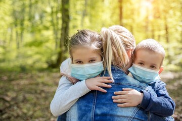 Mother hugging her children wearing medical face masks to be protected from COVID-19 virus