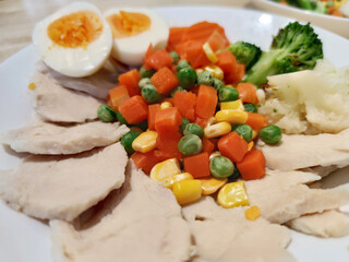 sliced Streamed organic chicken breast serving with sliced medium boiled egg and various vegetables corn carrot peas Broccoli on white flat plate, homemade, fresh market restaurant, food menu advertis