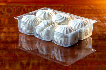 Six white marshmallows in plastic box reflex in polish wood table. Dessert is very sweet but unhealthy, unnatural and contain many sugar. Landscape image with beautiful brown background.