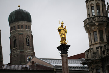 Fototapeta na wymiar Golden scuplture of Virgin Mary at Marienplatz with Both onion domes of the Gothic cathedral backgrounds, Munich, Germany, Travel Destinations