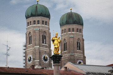 Fototapeta na wymiar Golden scuplture of Virgin Mary at Marienplatz with Both onion domes of the Gothic cathedral backgrounds, Munich, Germany, Travel Destinations