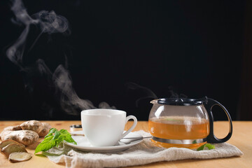 Cup of hot ginger tea and mint with steam from cup on wooden table over black background. the...