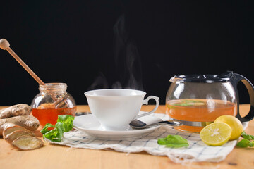 Cup of hot ginger tea with honey, lemon and mint with steam from cup on wooden table over black background. the concept of natural medicine.