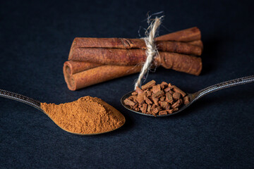 Cinnamon on a black background. A spoonful of young cinnamon lies next to a spoonful of crushed...