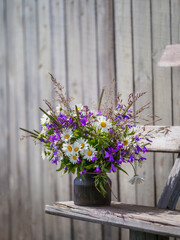 Bouqet with wild flowers on old wooden bench. Field flowers bouqet with campanula and camomile. Cottagecore and farmcore concept. Copy space