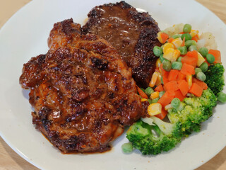 Sliced Grilled organic pork, beef Ribeye steak decorated with various colorful vegetables dressing corn carrot peas lemon serving on white plate on wooden table, One famous menu of secret recipe from 
