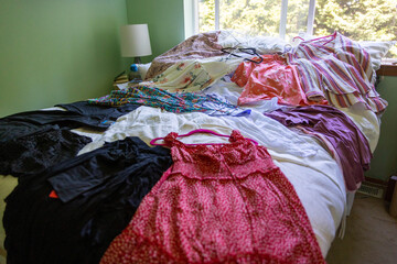 Clothes including dresses displayed on bed to pack for a vacation trip