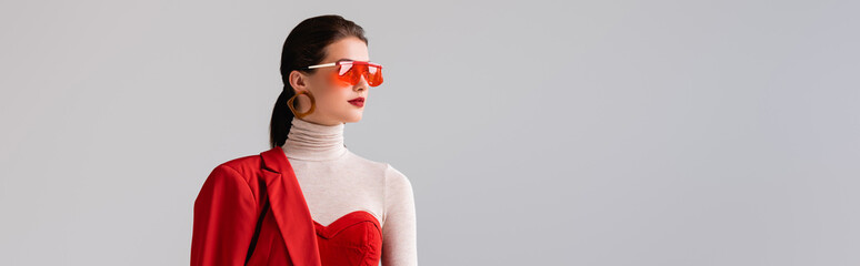 panoramic shot of elegant girl in red sunglasses looking away isolated on grey