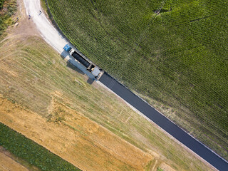 Aerial drone view. Construction of an asphalt road next to a green corn field in the countryside in...