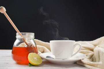 Cup of hot honey lemon tea and mint with steam from cup on wooden table with dressed in knitted warm winter scarf over black background. the concept of natural medicine.