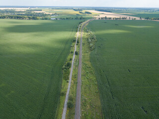 Railroad through a green corn field in Ukraine. Aerial drone view.