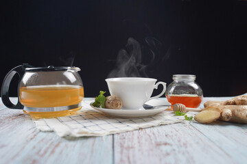 Cup of hot ginger tea with honey and mint with steam from cup on wooden table over black background. the concept of natural medicine.