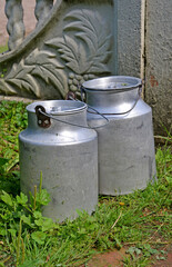 Two milk bidons stand on grass in the yard