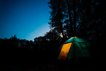 Glowing blue tent in the forest under a starry evening sky. Sunset in forest. Summer landscape.