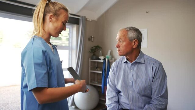 Young female doctor in scrubs discussion results with elderly male patient on digital tablet