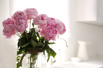 Vase with bouquet of beautiful pink peonies in kitchen, closeup