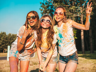 Three happy beautiful girls making party at Holi colors festival in summer time.Young smiling women friends having fun after music event at sunset. Positive models going crazy in sunglasses at sunset