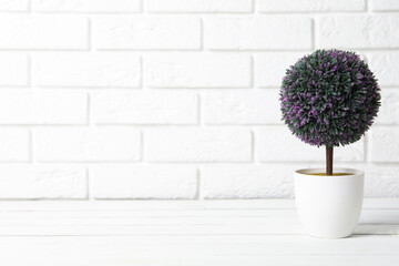 Beautiful artificial plant in flower pot on white wooden table near brick wall. Space for text