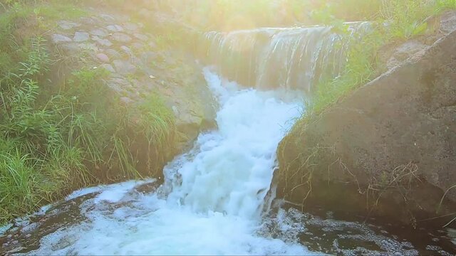 Beautiful sunny waterfall of a mountain river. Old stone bridge with seething water