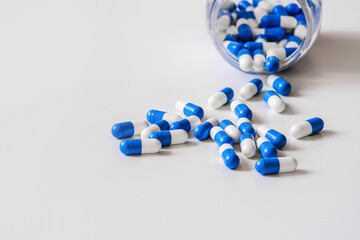 Capsules of the drug, white and blue in color, are scattered from a jar on the table. High-resolution photos. Macro photography with selective focus.