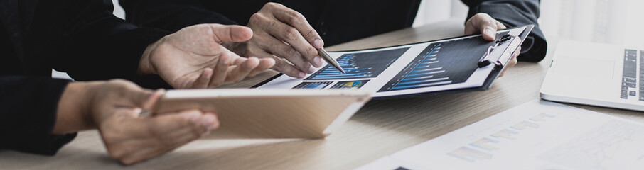 Young man in a black suit is analyzing financial graphs with a black woman in the office.