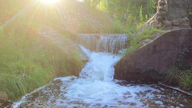 Beautiful sunny waterfall of a mountain river. Old stone bridge with seething water