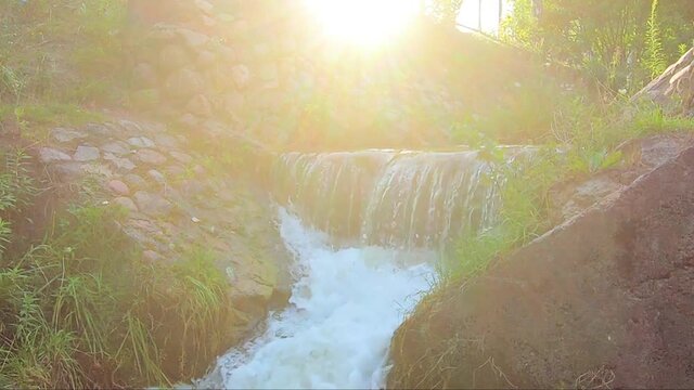 Beautiful sunny waterfall of a mountain river. Old stone bridge with seething water