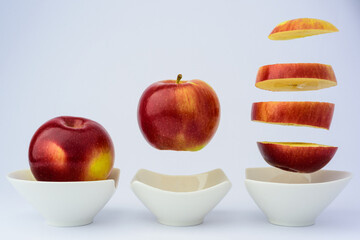 A red apple whole, levitating over a cup and cut into large pieces also levitating over a cup