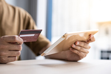 Asian man is holding a credit card and paying with a tablet.