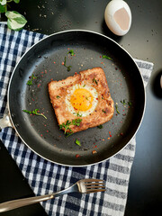 Egg in a hole topped with chili flakes, oregano, and herbs on a pan.