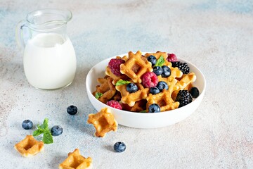 Tiny (Mini) waffles waffles with milk for breakfast with berries in a white bowl on a light background.