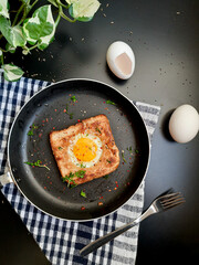 Egg in a hole topped with chili flakes, oregano, and herbs on a pan.